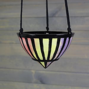 May include: A hanging ceramic planter with a black rim and a colorful striped design in shades of pink, yellow, and purple. The planter is suspended by black rope.