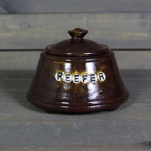 May include: A brown ceramic jar with a lid, featuring the word "REEFER" spelled out in white letters on the front.