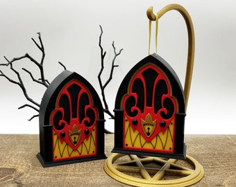 May include: Two black and red gothic-style door ornaments with gold accents. The ornaments are hanging from a gold stand with a pentagram design.