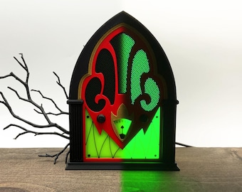 May include: A gothic-style arched lamp featuring a black frame with red accents and a green illuminated panel. The design includes a central gauge and decorative cutouts. The text LAMP OFF appears on the left and LAMP ON on the right.