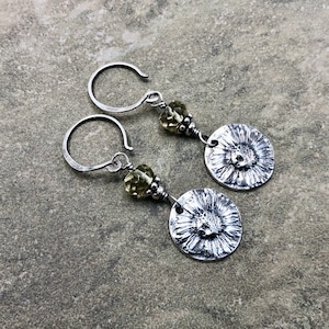 May include: A pair of silver earrings with a textured flower design and a light green gemstone bead on each earring.