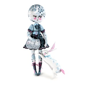 K&ouml;nnte beinhalten: Eine skurrile Puppe mit rundem Kopf und floral gemustertem Kleid, die eine Handtasche mit einem schlafenden Katzenmuster h&auml;lt. Ein wei&szlig;es Kaninchen mit rosa Ohren und floralen Akzenten steht neben der Puppe. Das Gesicht der Puppe hat rosige Wangen und einen ruhigen Ausdruck.