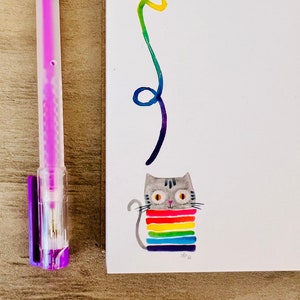 May include: A gray cat wearing a rainbow striped sweater with a rainbow line drawn above it.