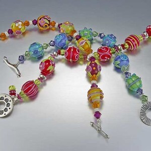 Pode incluir: Um colar multicolorido de várias camadas com fechos de prata e contas com padrões florais e em espiral. As contas são de vidro e estão em tons de vermelho, laranja, amarelo, verde, azul e roxo.