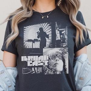 Peut inclure: T-shirt gris foncé avec un imprimé collage en noir et blanc. Le motif comprend une scène de performance et le mot "BROADCAST" en gras.