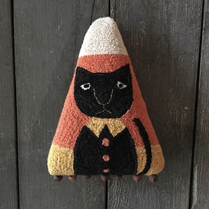 Peut inclure: Décoration d'Halloween triangulaire faite à la main ressemblant à un chat en bonbon de maïs. Le chat a un visage et un corps noirs, avec des sections orange, jaune et crème. Le chat a une expression triste et est décoré de petites cloches.
