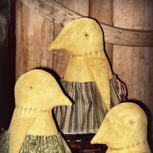 Könnte beinhalten: Drei handgefertigte Osterküken-Puppen mit gelben Körpern und Stoffröcken. Die Röcke weisen grüne und schwarze Muster auf. Die Puppen werden vor einem hölzernen Hintergrund ausgestellt. Der Text "Bess - Dressed Easter Chick" steht oben.