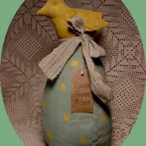Könnte beinhalten: Handgefertigte Osterdekoration mit einer hellblauen, eiförmigen Form mit gelben Tupfen. Auf dem Ei sitzt ein gelber Vogel, und ein Anhänger trägt die Aufschrift "Easter Thyme Blues". Die Dekoration ist mit einem gestreiften Band gebunden.