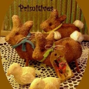 Könnte beinhalten: Handgefertigte rustikale Osterdekorationen mit drei braunen Hasenfiguren mit weißen Baumwollschwänzen und zwei gelben Kükenfiguren. Die Hasen haben blaue und gelbe Schleifenakzente. Das Bild enthält den Text "Sassafras Hill Primitives".