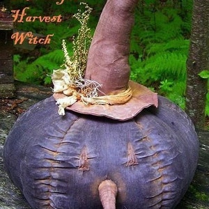 Könnte beinhalten: Handgefertigte Hexendekoration mit einem dunkelvioletten Körper und gestickten Details. Sie hat eine lange, spitze Nase und einen braunen, spitzen Hut mit breiter Krempe. Der Text "Autumn Moonlight Harvest Witch" ist sichtbar.