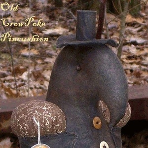 May include: A handmade crow pincushion with a black fabric body, a brown fabric pincushion, and a black top hat. The pincushion is labeled "Old Crow Poke Pincushion".