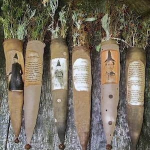 May include: Six tan fabric cone-shaped pouches labeled Witchy Potion Pockets, each containing dried herbs. The pouches feature printed vintage-style portraits of figures in pointed hats or text blocks, and each has a small metal bell at the bottom tip.