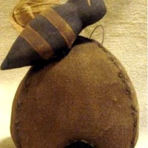 May include: A fabric bee figurine with black and brown stripes and wire antennae perched atop a round, brown fabric beehive structure. The beehive features visible stitched seams along its sides and a small, circular black opening at the base.