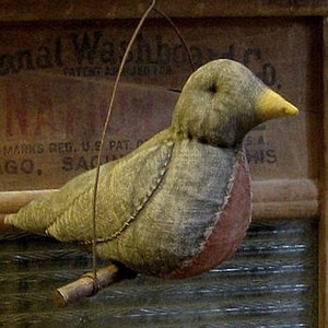 May include: A handcrafted, rustic-style fabric bird ornament, a "Prim Olde Robin Hanger," with a green body, red breast, and yellow beak. The bird is perched on a wooden branch and suspended by a wire. The background includes text from "National Washboard Co."