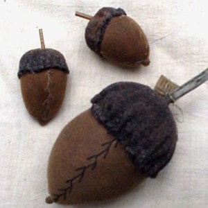 May include: Three brown fabric acorns with black stitching. The acorns are handmade and have a rustic look.