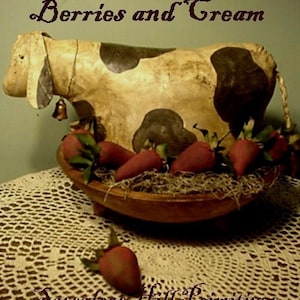 Op de afbeelding: Een handgemaakte koeienfiguur met zwarte vlekken en een bel, achter een houten kom gevuld met rode aardbeien. De teksten "Berries and Cream" en "Sassafras Hill Primitives" zijn zichtbaar, wat een rustieke uitstraling oproept.