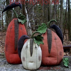 May include: Three handcrafted fabric pumpkins in orange and cream, with dark grey detailing and green leaves. Each pumpkin features a stitched face and a curved black handle. The text "Dam-Funfolks" is visible at the top.