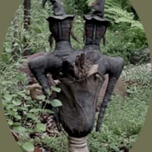 Könnte beinhalten: Zwei schwarze Hexenpuppen mit spitzen Hüten und langen schwarzen Kleidern stehen in einer Gartenlandschaft. Die Puppen halten einen Jutesack und einen Stock. Der Text "Witchy Sisters Make-Do" befindet sich oben im Bild und "Sassafras Hill Primitives" unten.