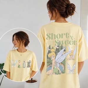May include: A pale yellow t-shirt featuring a graphic of a fairy, wings, a potion bottle, and a small tower on the front. The back displays a large illustration of a fairy with the text Short N Sweet and the phrase I leave quite an impression.