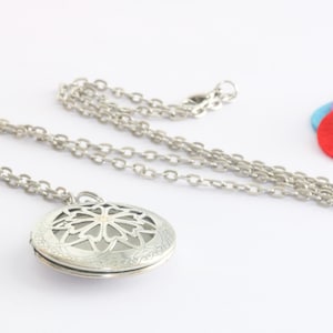 Könnte beinhalten: Halskette mit silberfarbenem Medaillon mit floralem Design. Das runde Medaillon hängt an einer Kette. Drei farbige Filzkreise in Rosa, Rot und Blau sind ebenfalls im Bild.