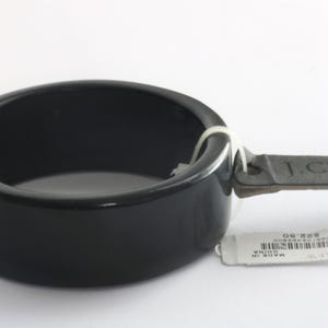 Op de afbeelding: Een zwarte keramische armband met een leren handvat. De armband is rond en heeft een glanzende afwerking. Een wit label is aan het handvat bevestigd. Het label heeft de tekst "J.CREW" en een barcode.