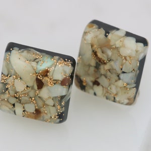 May include: A pair of square-shaped earrings with a black background and a design of small white and brown stones and gold glitter.