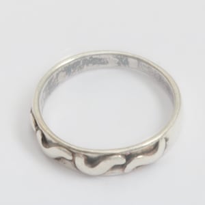 May include: A silver ring with a wavy pattern around the band. The ring has a simple, elegant design and appears to be made of sterling silver. The ring is shown against a white background.