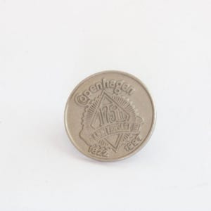Puede incluir: Una moneda conmemorativa de color plateado. La moneda presenta el texto "Copenhague" en la parte superior, con "175th Anniversary" en el centro y los años "1822" y "1997" en la parte inferior. La moneda tiene forma circular.