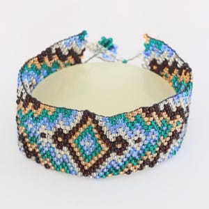 May include: A beaded bracelet with a geometric pattern in shades of blue, green, brown, and gold.