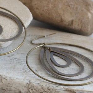 May include: A pair of gold-toned earrings with a layered, teardrop design. The earrings are made of metal and have a simple, elegant style.