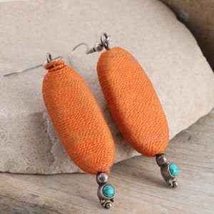May include: A pair of orange fabric earrings with turquoise stones and silver accents.