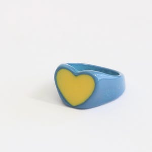 Puede incluir: Un anillo azul con un diseño de corazón amarillo.