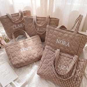May include: A collection of five quilted tote bags in a brown and white gingham pattern. Each bag features two handles and is embroidered with a unique name in white thread, specifically the names Clara, Ollie, Nora, Finn, and Liza.