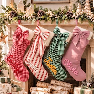 Puede incluir: Cuatro calcetines de Navidad colgados en fila. El primero es de cuadros rojos con un lazo rojo y el nombre Emily. El segundo es de rayas rojas y blancas con un lazo a rayas y el nombre Sophie. El tercero es de cuadros verdes con un lazo verde y el nombre Justin. El cuarto es rosa liso con un lazo rosa y el nombre Olivia.