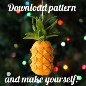 May include: A felt pineapple decoration with a green crown and a yellow body, hanging against a blurred background with colourful lights. The image includes the text "Download pattern and make yourself!"