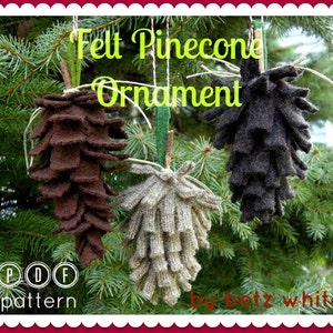 Op de afbeelding: Drie vilten dennenappelornamenten in bruin, grijs en zwart hangen aan touw tegen een achtergrond van groenblijvende takken. De tekst "Felt Pinecone Ornament" staat in groen geschreven. De afbeelding bevat ook de tekst "PDF pattern".