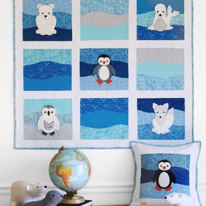 May include: A sewing pattern for a quilt and pillow set featuring a polar bear, penguin, owl, and arctic fox. The quilt is white with blue and gray squares. The pillow is white with a blue penguin on it. The pattern is called "Polar Babies Quilt & Pillow" by "betz white".