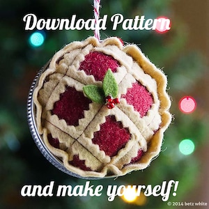 Peut inclure: Une décoration de Noël en feutre en forme de tarte avec une garniture rouge et une croûte beige. La décoration est ornée d'une feuille de houx en feutre vert et de perles rouges. Le texte "Download Pattern and make yourself!" est visible en bas de l'image.
