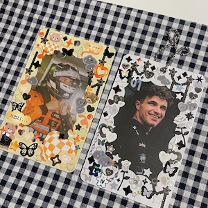 May include: Two white cardstock photo holders with black and white borders decorated with stickers. The left holder features a photo of a race car driver wearing a helmet and a yellow and orange racing suit. The right holder features a photo of a man with curly brown hair wearing a black and white racing uniform. The text "진짜 재밌어..." is on the left holder and "01" is on the right holder.
