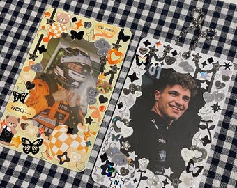 May include: Two white cardstock photo holders with black and white borders decorated with stickers. The left holder features a photo of a race car driver wearing a helmet and a yellow and orange racing suit. The right holder features a photo of a man with curly brown hair wearing a black and white racing uniform. The text "진짜 재밌어..." is on the left holder and "01" is on the right holder.