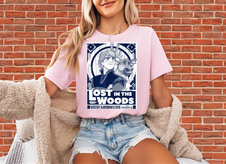 Puede incluir: Camiseta rosa claro con un dise&ntilde;o de la pel&iacute;cula Frozen II. El dise&ntilde;o es una ilustraci&oacute;n azul y blanca de Kristoff, Sven el reno, y el texto "LOST IN THE WOODS".