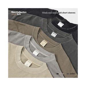 K&ouml;nnte beinhalten: F&uuml;nf kurz&auml;rmelige T-Shirts in verschiedenen neutralen Farbt&ouml;nen, von Schwarz bis Beige. Die Shirts sind diagonal angeordnet, wodurch ihre Rundhalsausschnitte hervorgehoben werden. Der Text "New Collection 2025 S/S" und "Wash and make old short sleeves" ist ebenfalls zu sehen.