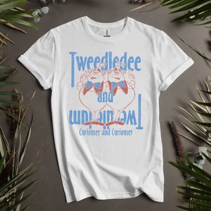 Könnte beinhalten: Weißes T-Shirt mit einer Grafik im Vintage-Stil von Tweedledee und Tweedledum aus Alice im Wunderland. Der Text lautet "Tweedledee and Tweedledum" mit dem Satz "Curiouser and Curiouser" darunter.