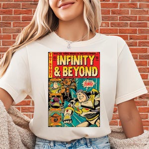 Puede incluir: Camiseta color crema con un dise&ntilde;o gr&aacute;fico estilo c&oacute;mic. El dise&ntilde;o presenta las palabras "INFINITY & BEYOND" y personajes de dibujos animados. Tambi&eacute;n se ve la palabra "ZURG!"