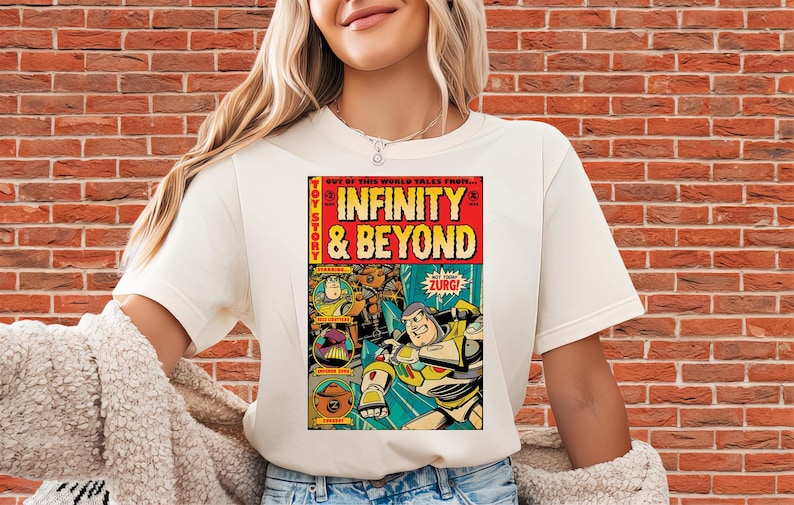 Puede incluir: Camiseta color crema con un dise&ntilde;o gr&aacute;fico estilo c&oacute;mic. El dise&ntilde;o presenta las palabras "INFINITY & BEYOND" y personajes de dibujos animados. Tambi&eacute;n se ve la palabra "ZURG!"