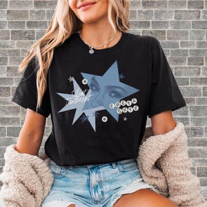 Puede incluir: Camiseta negra con un diseño de estrella azul, el texto "Silent Treatment" y "Freya Skye". La estrella contiene una imagen azul de ojos. Una prenda casual.