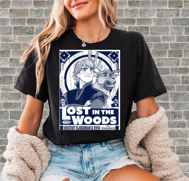 Puede incluir: Camiseta negra con un dise&ntilde;o gr&aacute;fico de la pel&iacute;cula de Disney Frozen II. El dise&ntilde;o incluye el texto "LOST IN THE WOODS" con im&aacute;genes de Kristoff, Sven y elementos decorativos en blanco y azul marino.