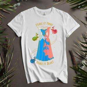 May include: White t-shirt with a colourful illustration of a dress split in two, one side blue and the other pink, with the text "MAKE IT PINK! MAKE IT BLUE!". The design includes fairy characters and gold accents.