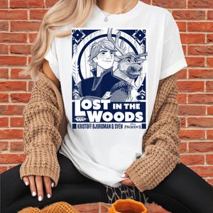 Puede incluir: Camiseta blanca con un gr&aacute;fico azul y blanco de Kristoff y Sven de Frozen II, con el texto "LOST IN THE WOODS". La camiseta tambi&eacute;n incluye el texto "KRISTOFF BJORGMAN & SVEN FROZEN II".