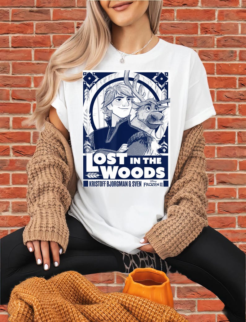 Puede incluir: Camiseta blanca con un gr&aacute;fico azul y blanco de Kristoff y Sven de Frozen II, con el texto "LOST IN THE WOODS". La camiseta tambi&eacute;n incluye el texto "KRISTOFF BJORGMAN & SVEN FROZEN II".